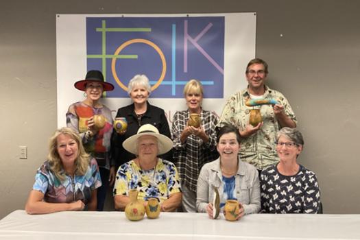 A group of people pose with their handmade creations in front of the Rocky Mountain Folk School banner