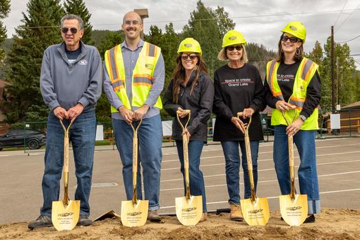 Group of people wear hard hats and hold golden shovels ready for a ceremonial groundbreaking.